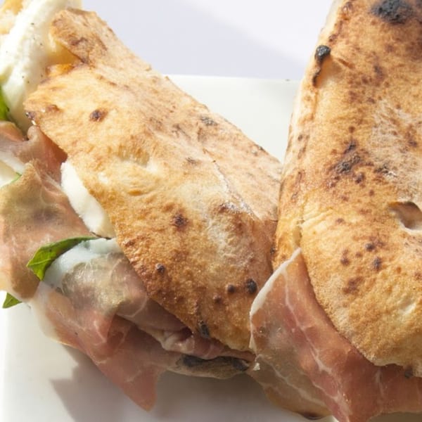 Two calzones filled with prosciutto, fresh mozzarella, and basil on a white plate.