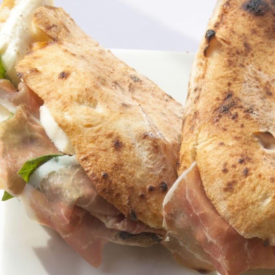 Two calzones filled with prosciutto, fresh mozzarella, and basil on a white plate.