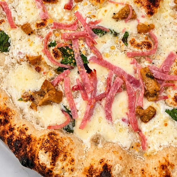 Close-up of a white pizza with melted cheese, spinach, mushrooms, and thin strips of red meat.