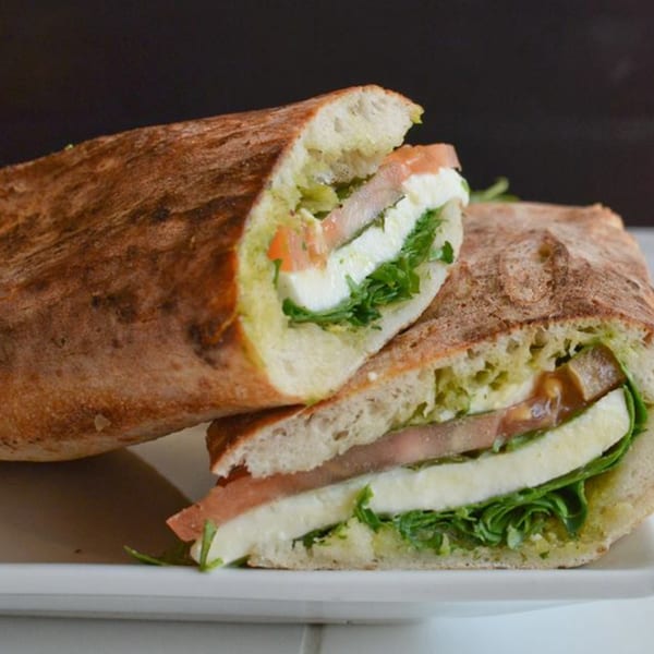 Two halves of a Menomale sandwich filled with mozzarella, prosciutto, pesto, and arugula.