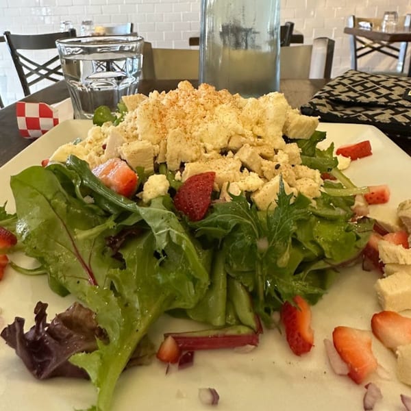 A fresh salad with mixed greens, strawberries, and crumbled cheese on a white plate at Menomale.