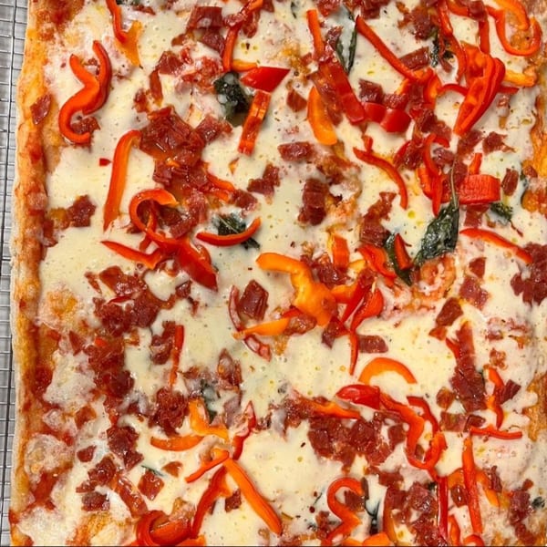 Close-up of a rectangular pizza with melted cheese, red peppers, and crumbled pepperoni.