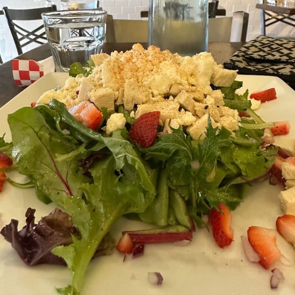 A fresh salad with mixed greens, strawberries, and crumbled cheese on a white plate at Menomale.