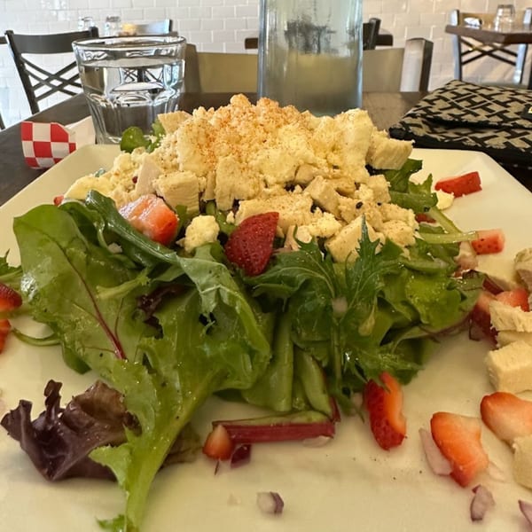 A fresh salad with mixed greens, strawberries, and crumbled cheese on a white plate at Menomale.
