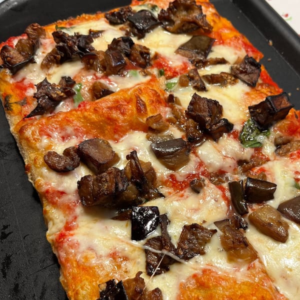 Close-up of a rectangular pizza with melted cheese, tomato sauce, and roasted eggplant pieces.