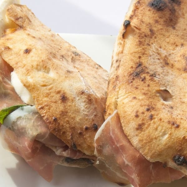 Two golden-brown calzones, one revealing prosciutto, mozzarella, and basil, on a white plate.