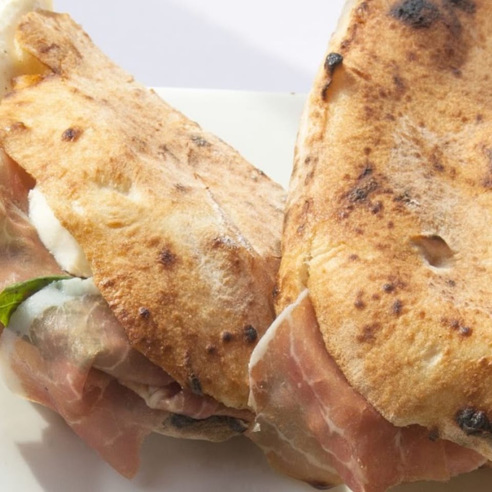 Two golden-brown calzones, one revealing prosciutto, mozzarella, and basil, on a white plate.