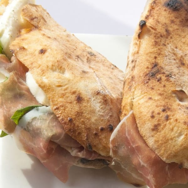 Two calzones filled with prosciutto, fresh mozzarella, and basil on a white plate.
