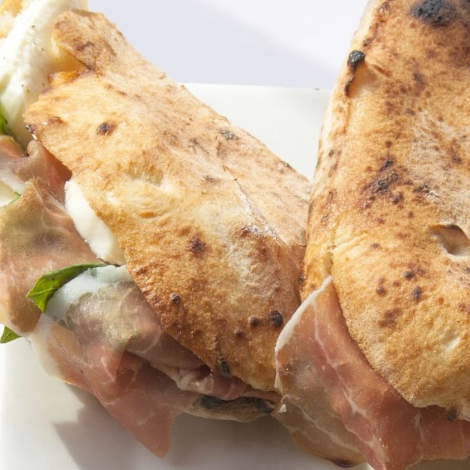 Two calzones filled with prosciutto, fresh mozzarella, and basil on a white plate.